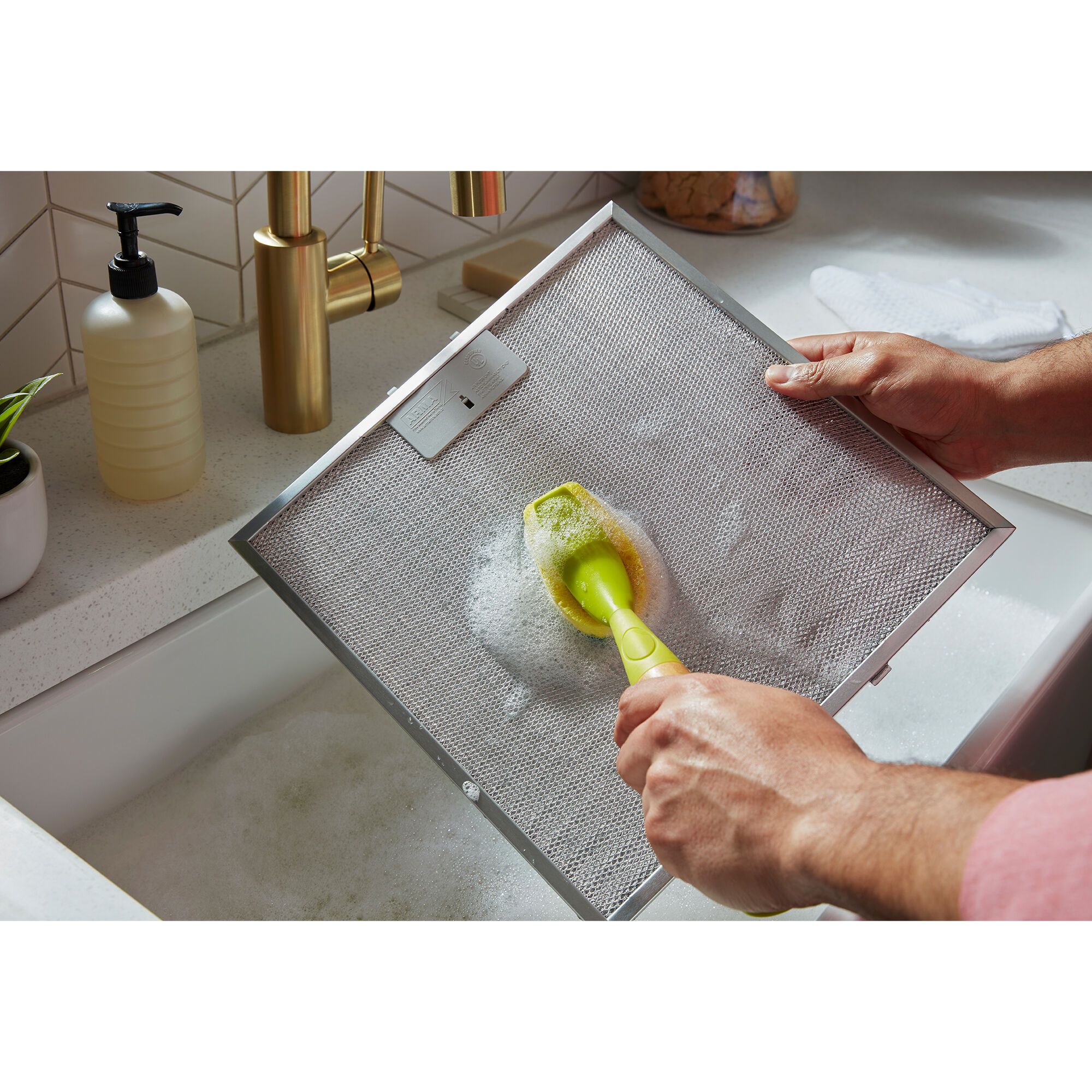 Removable grease filter being unlatched from the Whirlpool WVW53UC0LS range hood for cleaning at the sink.