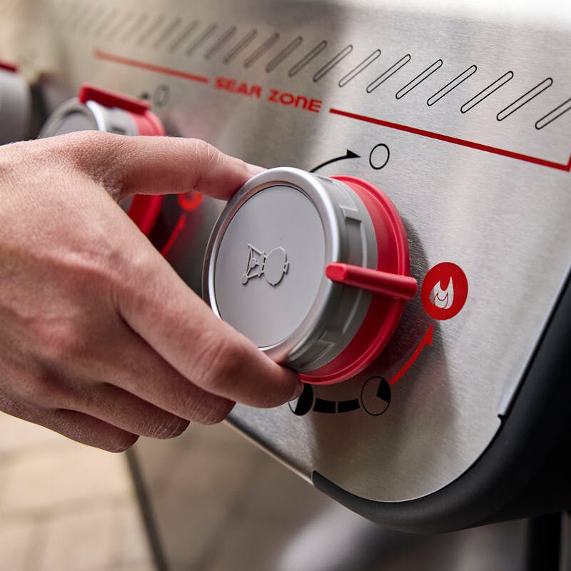 Weber Spirit E-425C - close-up of a hand turning the Sear Zone burner knob on a stainless steel Weber gas grill.