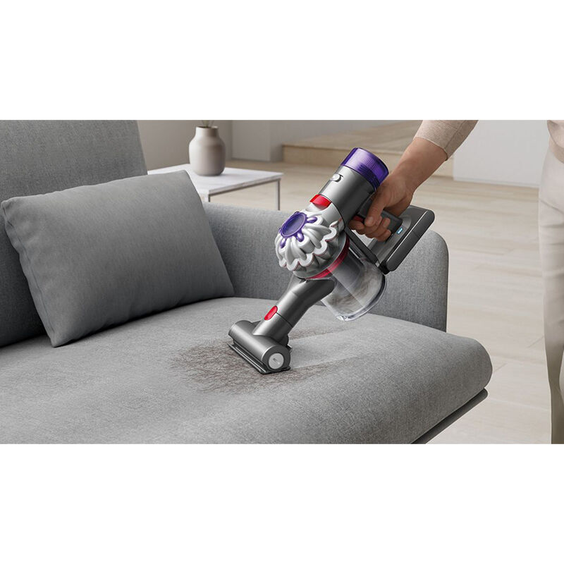 Dyson Mini Motorhead attachment being used on a fabric sofa surface, showing the motorized brush bar agitating and lifting embedded dirt and pet hair.