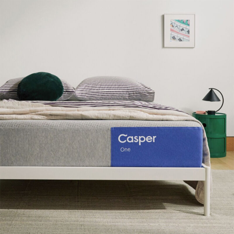 Casper One foam mattress on a white metal bed frame with striped and round pillows, styled in a modern bedroom.