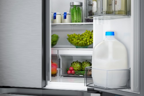 Close-up of Midea French door refrigerator interior showing organized shelves with fresh grapes, vegetables, fruits, a gallon of milk, and condiments stored in the door bin.