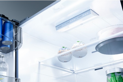 Close-up of Midea French door refrigerator interior ceiling showing bright LED lighting panel and control display, with egg holders and beverages stored on upper shelves.