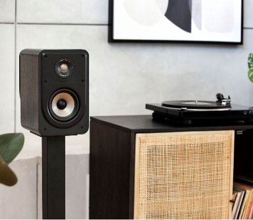 Single Polk Signature Elite ES15 black bookshelf speaker on stand beside record player and woven cabinet in modern living room setting