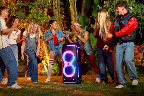 Group of friends dancing and laughing outdoors at night around the JBL PartyBox 720 speaker with colorful LED lights, creating a lively party atmosphere.