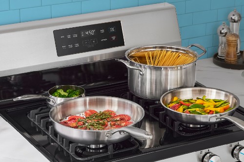 Midea oven cooktop with stainless steel pans cooking vegetables, meat, and pasta in a pot of boiling water.