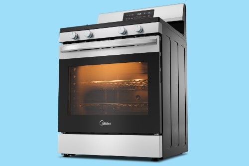 Midea freestanding stainless steel gas range with oven door closed, control knobs on top, and oven light glowing inside against a blue background.