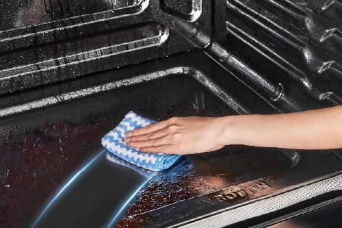 Hand with a blue patterned cloth wiping the interior floor of a Midea oven