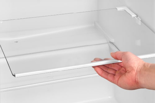 Hand removing clear plastic crisper drawer from compact refrigerator, demonstrating easy-access storage for fruits and vegetables.