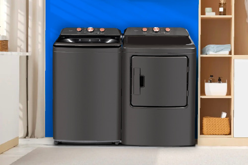 Midea top load washer and matching dryer side-by-side in metallic grey with rose gold controls, displayed in modern laundry room with blue accent wall.