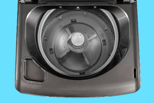 Top-down interior view of washer showing deep grey tub with central pulsator wash system, perforated drum design, and built-in fabric softener dispenser.