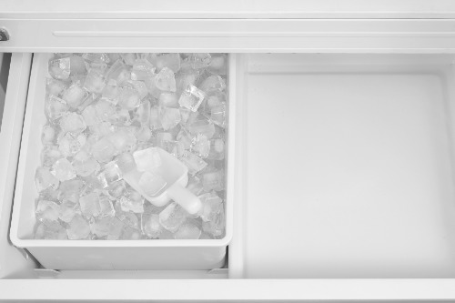 Close-up of the freezer drawer in Midea Refrigerator Model MRF23I5AST, showing an ice bin filled with ice cubes and scoop beside an adjacent storage compartment.