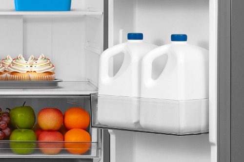 Close-up of Midea Refrigerator Model MRF23I5AST interior showing a door bin holding two gallon milk jugs, with nearby produce drawers and shelf storage.