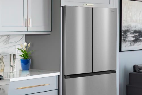 Midea Stainless steel French door refrigerator with counter-depth design in modern gray kitchen with white cabinets, marble backsplash, and contemporary decor. Bottom freezer drawer visible with black handle.
