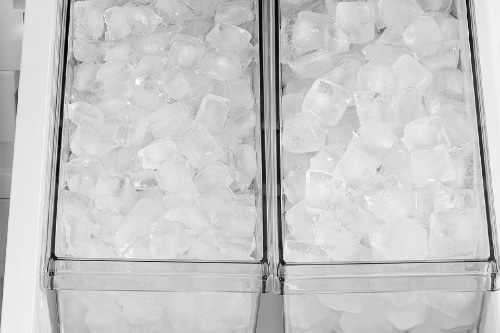 Two clear ice bins filled with cube ice in freezer drawer, showing dual storage compartments with metal handles for easy access and organization.