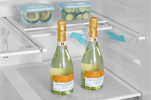 Two champagne bottles with gold foil tops on refrigerator shelf with split folding design and blue directional arrows. Food storage containers with sliced produce visible on upper shelf.