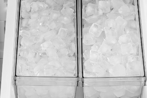 Close-up view of the Midea 32 cu. ft. French Door Refrigerator model MRF32I6BST freezer section showing two clear bins filled with fresh ice cubes, illustrating the refrigerator's ice storage capacity.