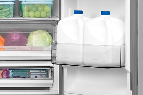 Interior view of the Midea 32 cu. ft. French Door Refrigerator model MRF32I6BST showing two large milk jugs stored in the door bin, highlighting spacious door storage for bulky beverage containers.