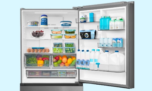 Interior view of Midea stainless steel bottom-freezer refrigerator with both doors open, showing spacious 23 cubic feet capacity filled with dairy, produce, beverages, and organized storage.