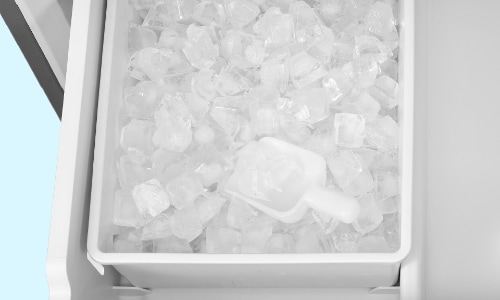 Overhead view of Midea refrigerator's spacious white ice maker drawer filled with fresh ice cubes and ice scoop, demonstrating ample ice production capacity.
