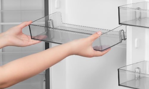 Hands removing clear plastic door bin from Midea refrigerator, demonstrating adjustable and removable storage compartments for easy cleaning and customization.