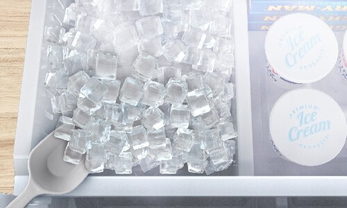 Overhead view of Midea refrigerator's spacious freezer drawer filled with ice cubes and ice cream containers, showing organized storage with ice scoop.