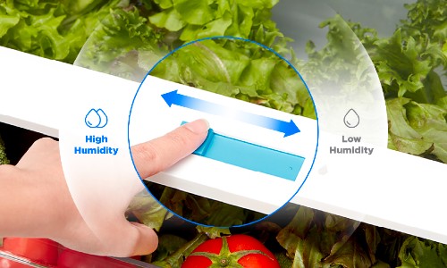 Hand adjusting humidity control slider on refrigerator crisper drawer with fresh lettuce and tomato visible, showing high to low humidity settings for optimal produce freshness.