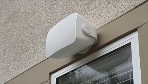 Sonos Outdoor Speaker model OUTDRWW1 in white mounted on an exterior wall above a window, designed for durable, weather-resistant performance in outdoor spaces.