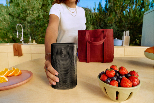 Woman placing Sonos Play speaker in black, set down on an outside picnic table.