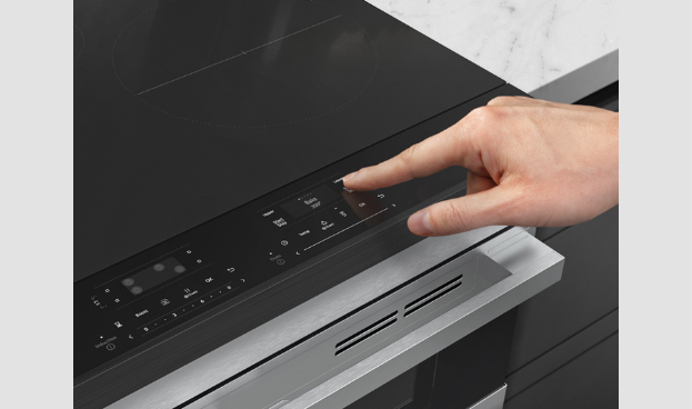Close-up of hand using Samsung range's sleek black glass touch control panel with stainless steel handle visible below on slide-in design.