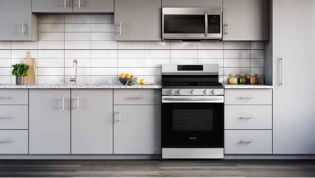 Samsung NX60A6111SS stainless steel gas range installed in modern kitchen with light gray cabinets, white tile backsplash, and matching stainless steel microwave.
