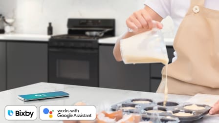 Person pouring batter into muffin tin with Samsung gas range in background, showing Bixby and Google Assistant logos indicating Wi-Fi and voice control compatibility.
