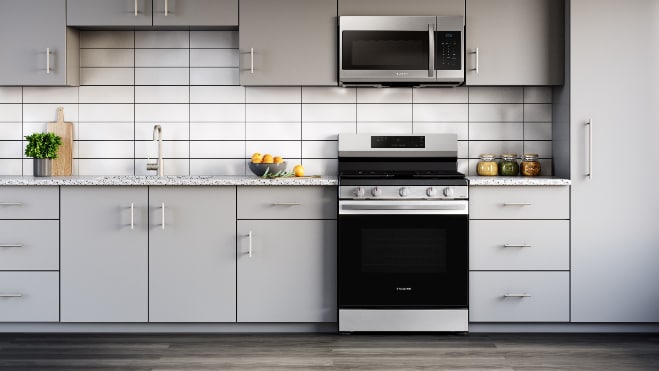 Samsung NX60A6311SS stainless steel gas range installed in modern kitchen with light gray cabinets, white tile backsplash, and matching stainless steel microwave
