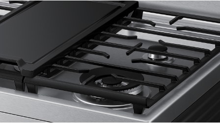 Close-up angled view of Samsung gas range cooktop showing black porcelain-coated continuous grates and dual brass burners on stainless steel surface.