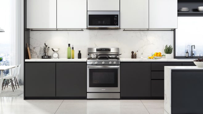 Samsung NX60A6711SS stainless steel gas range installed in modern kitchen with black and white cabinets, white countertops, and matching stainless steel over-the-range microwave