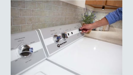 Close-up of hand adjusting control dial on Speed Queen white top-load washer with simple mechanical controls and lid open, showing user-friendly interface.