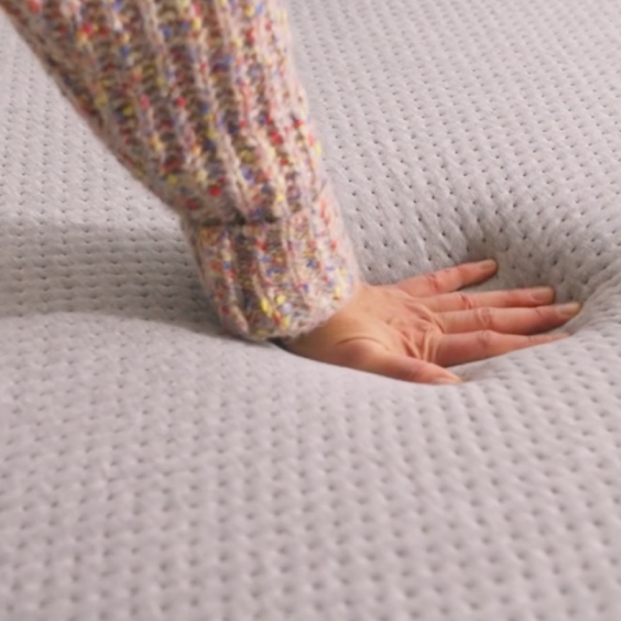 Hand pressing into Casper One mattress surface showing quilted white cover with textured dot pattern, demonstrating mattress comfort and responsiveness with hand sinking slightly into foam.