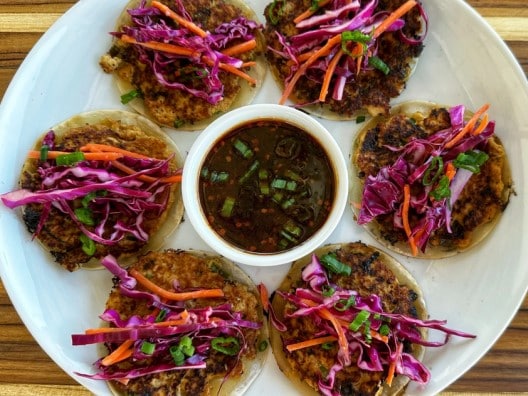 Overhead shot of plate with six unfolded tacos in a circle and a cup of dipping sauce in the middle