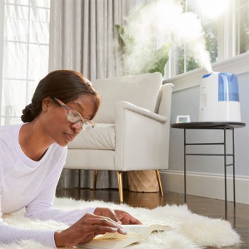 Woman Lounging on Shag Carpet Reading a Book While Humidifier Operates On Table in Background
