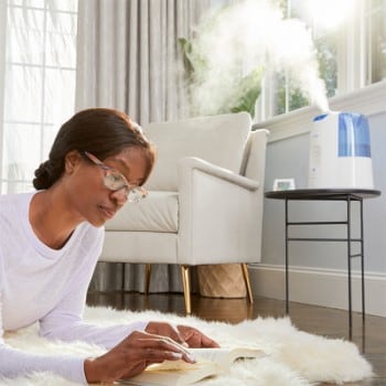 Woman Lounging on Shag Carpet Reading a Book While Humidifier Operates On Table in Background