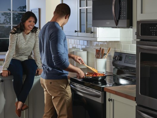 Woman in Kitchen with Man Cooking on Induction Stove