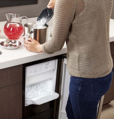 Woman Standing at Kitchen Counter Pouring Ice Into Ice Bucket with Open Undercounter Ice Maker Below