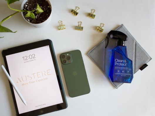Bottle of Austere Clean & Protect Cleaner on a desk with a tablet, phone, and scattered binder clips