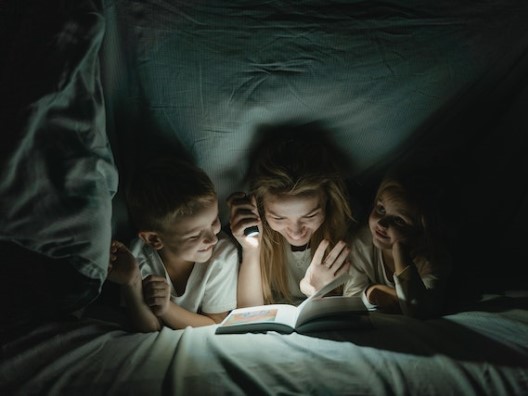 Kids and Mom Reading with Flashlight Under Blanket 