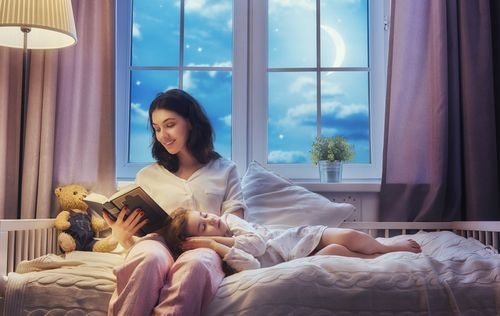 Mother reading to daughter in bed 