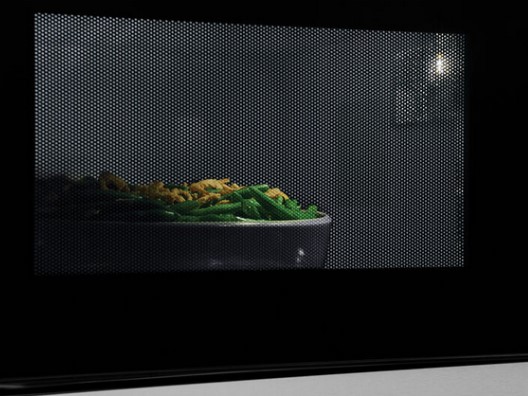 Casserole dish inside of microwave as seen through mesh grating on door window