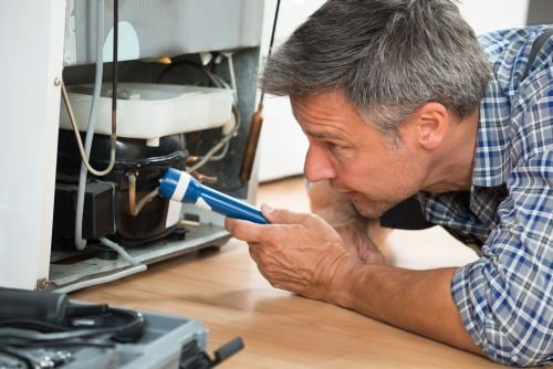 Man Examining Refrigerator with Flashlight