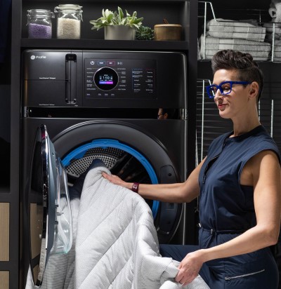 Person with light skin, short dark hair, and bright blue glasses removing comforter from GE Profile Ultrafast Combo Laundry Machine