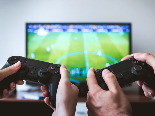 Two Pairs of Hands Operating Playstation Controllers in Front of a TV