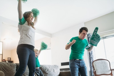 Man, Woman, and Toddler Cheering in Living Room with Sports Gear