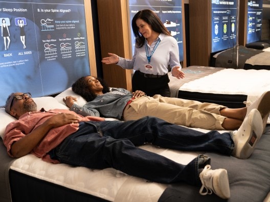 Couple in Mattress Showroom Lying on Mattress While Saleswoman Talks